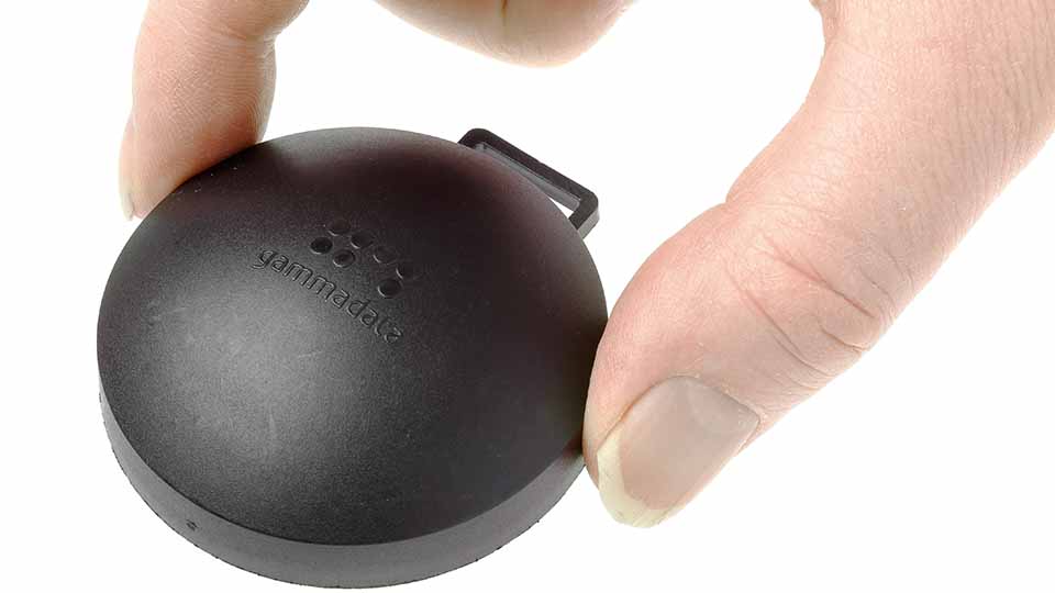 En hand som håller i en svart puck, som är en radonmätare.