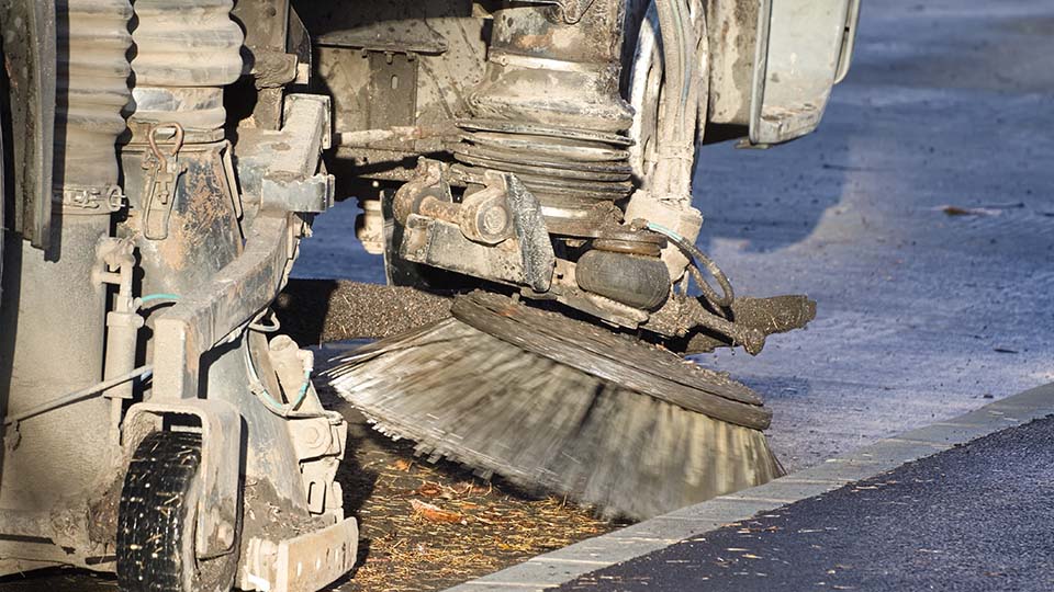 Närbild på en sopbilar som sopar upp grus och sand från gatan.
