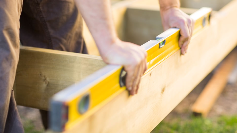 Person mäter med vattenpass på en bräda i trä. Foto. 