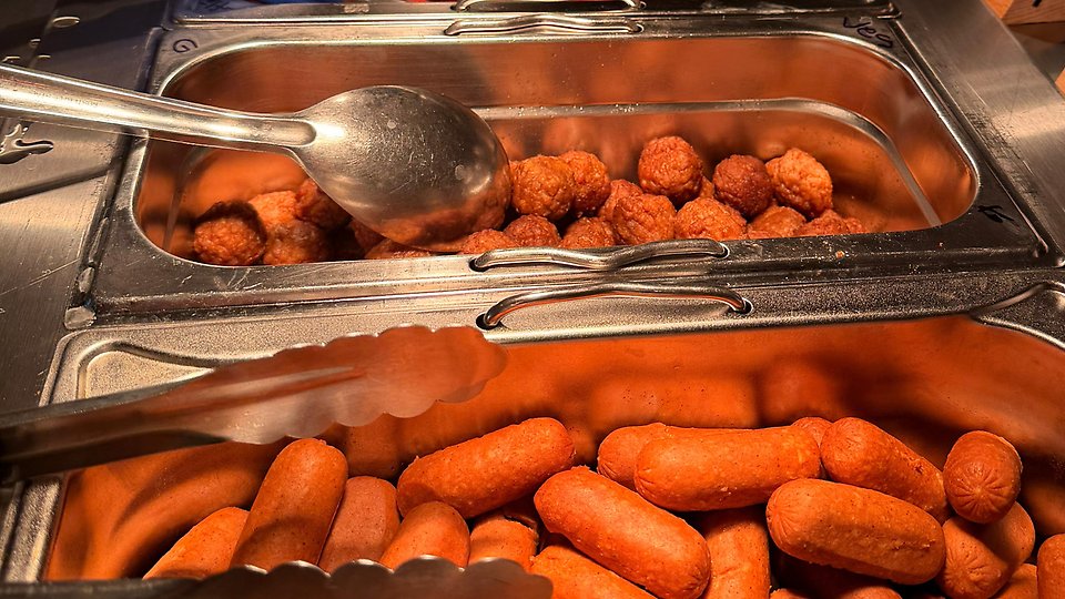 Buffé med korv och köttbullar i värmeskålar med serveringsbestick. Foto